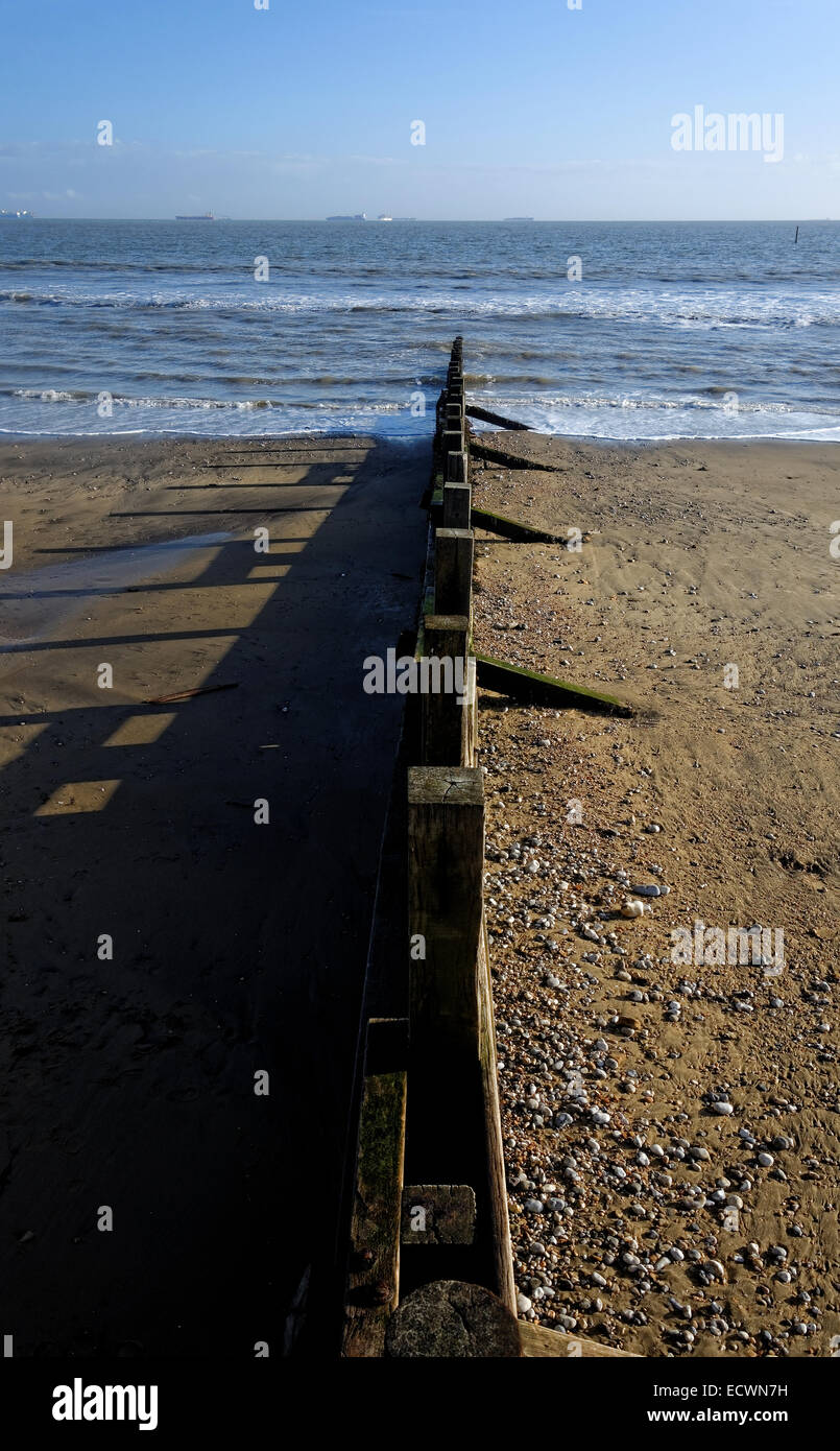 Un groyne creando profonde ombre sulla spiaggia di Sandown Bay, Isle of Wight con le navi in attesa di entrare in Southampton all'orizzonte Foto Stock