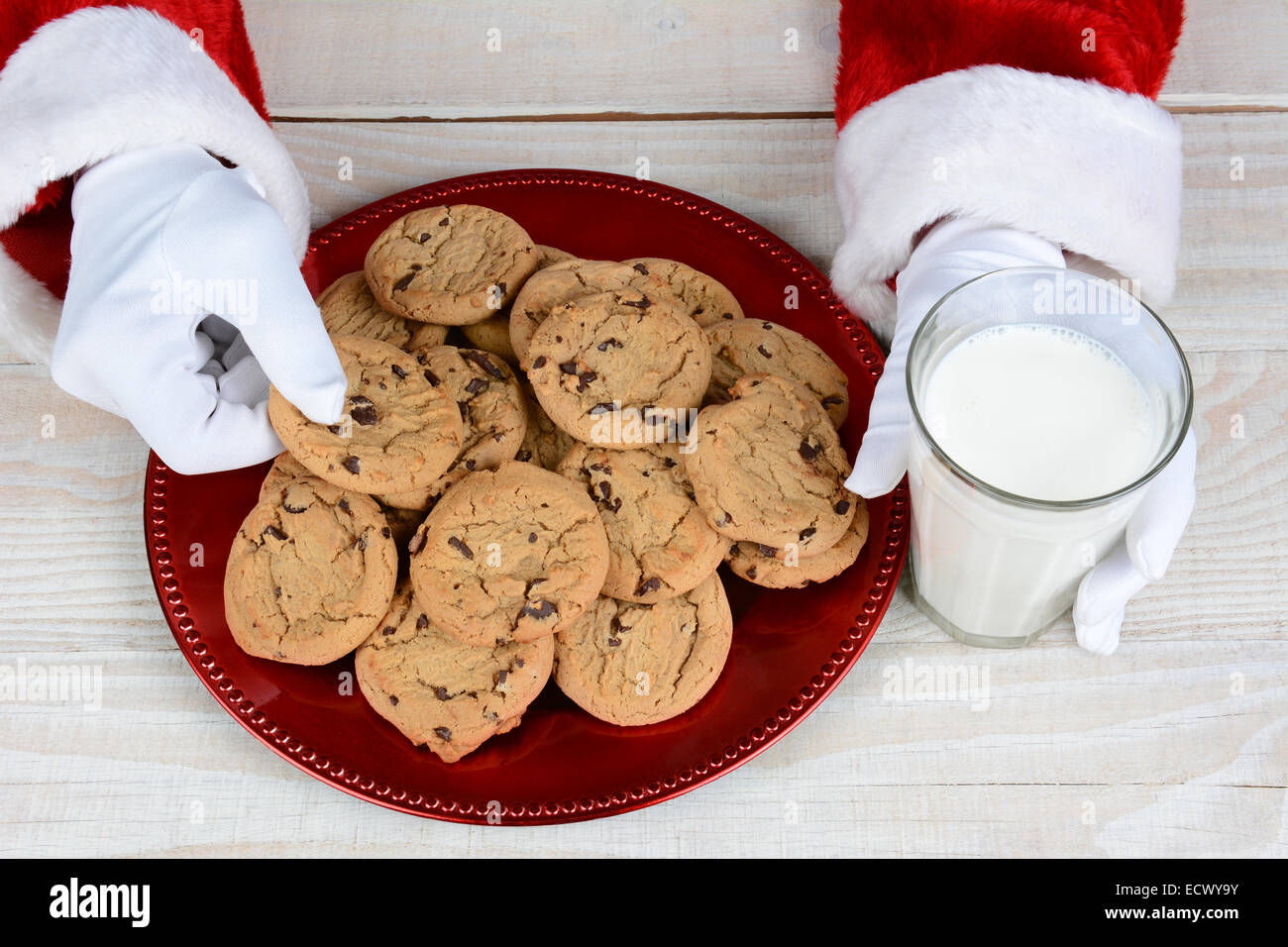 Primo piano di Babbo Natale con un piatto pieno di biscotti al cioccolato e un bicchiere di latte. Solo Santa le mani sono visibili. Foto Stock