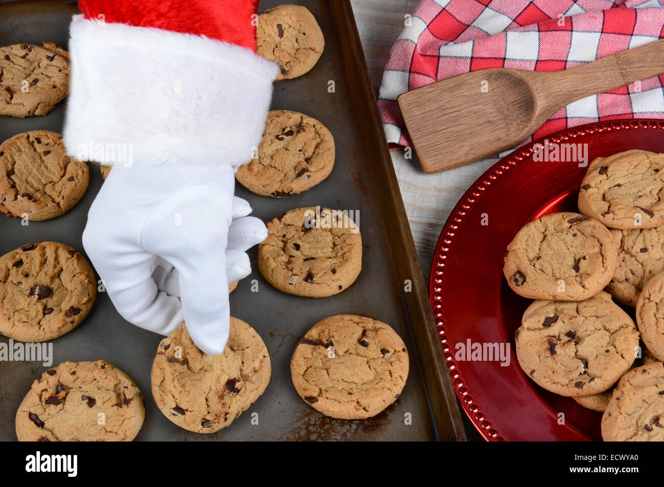 Primo piano di Santa Claus prendendo un fresco Biscotto cotto al forno da una placca da forno. Una piastra di biscotti al cioccolato è a lato. Foto Stock