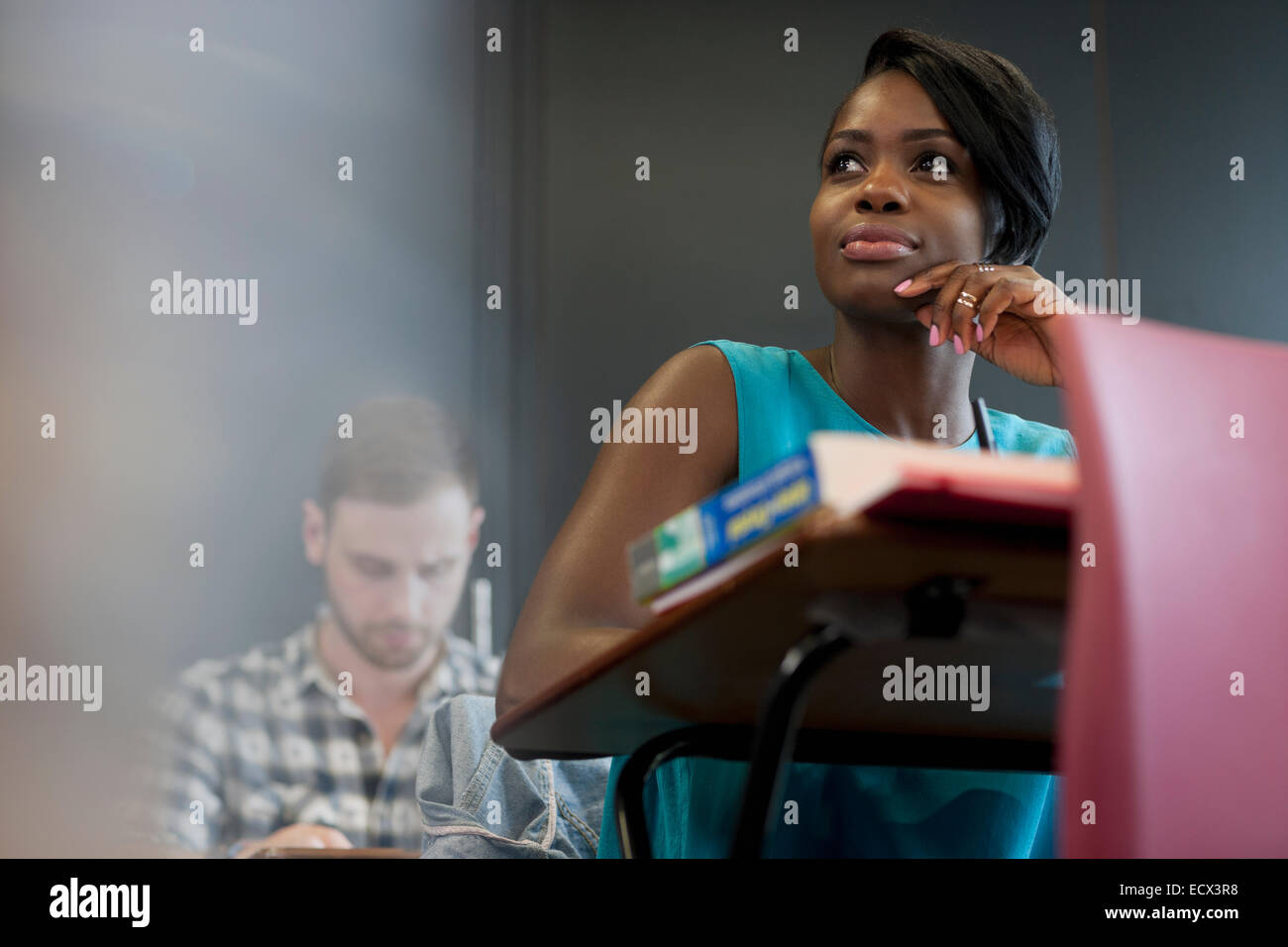 Studente universitario seduto alla scrivania con la mano sul mento Foto Stock