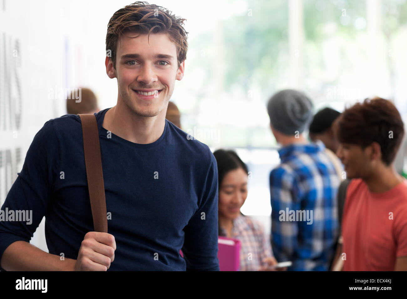 Ritratto di sorridere studente universitario in piedi in corridoio durante la pausa le persone a parlare di sfondo Foto Stock