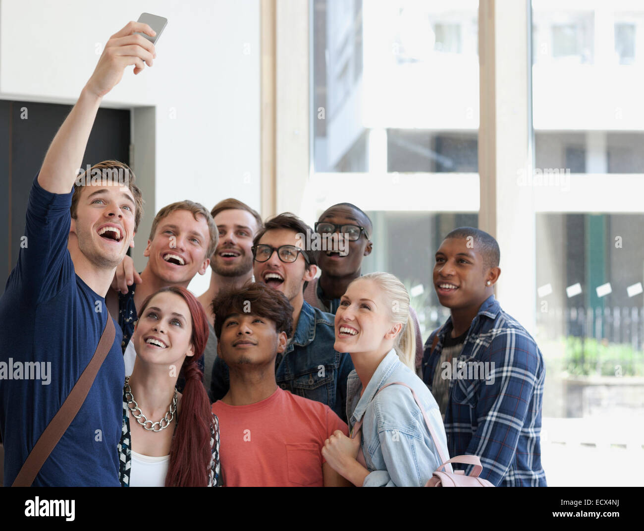 Gruppo di ridere studenti prendendo selfie sul corridoio con grande finestra in background Foto Stock