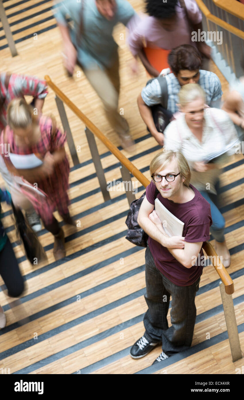 Ritratto di giovane maschio gli studenti titolari di Notes in piedi sulle scale con altri studenti di andare fino Foto Stock