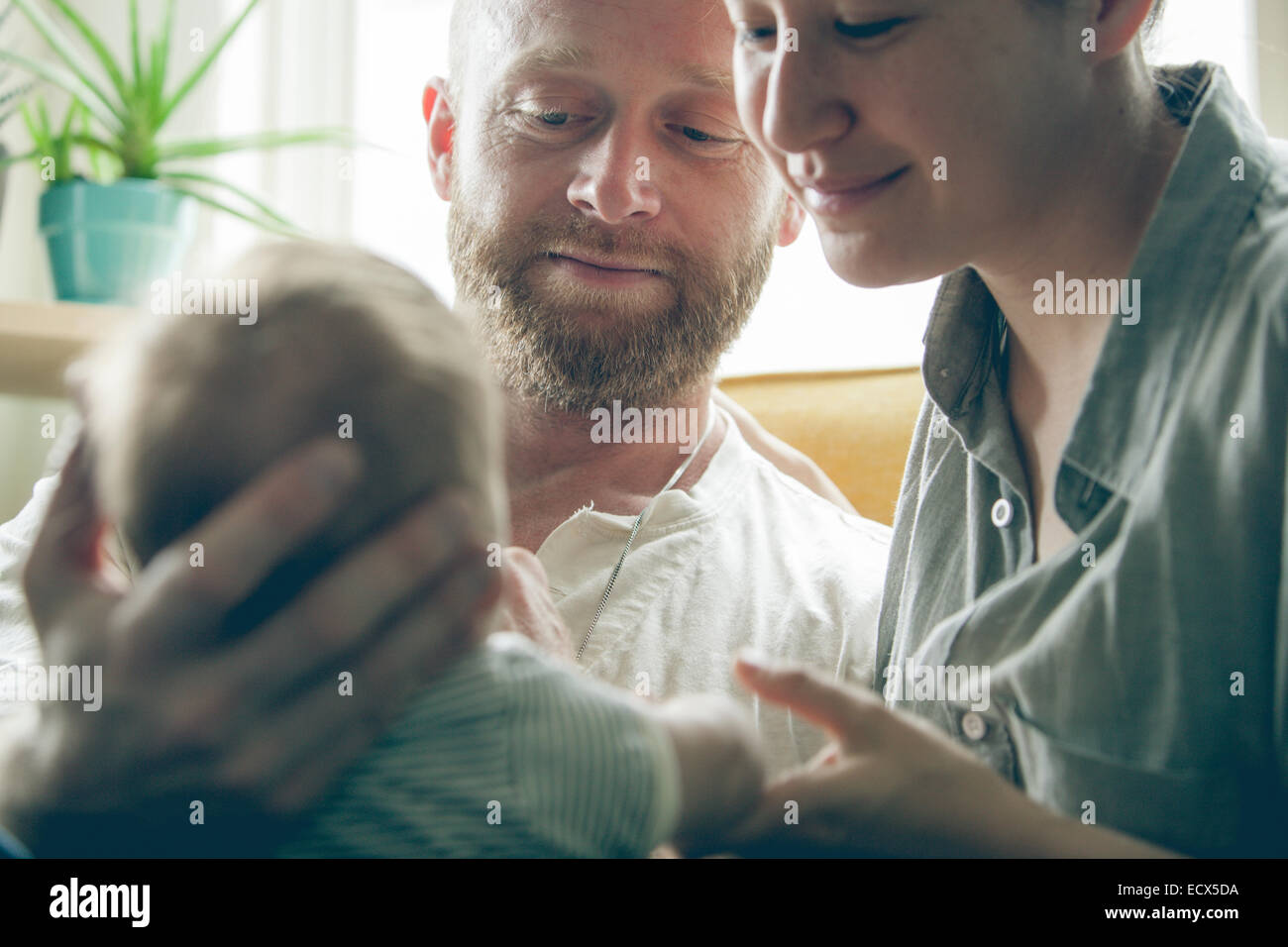 Vista dei genitori sorridente e azienda piccolo bambino seduto accanto alla finestra Foto Stock