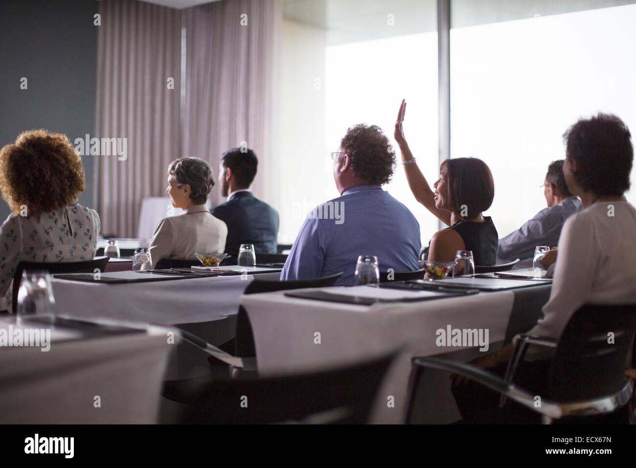 Media gruppo di partecipanti alla conferenza seduti nella sala conferenze con la donna alzando la mano Foto Stock