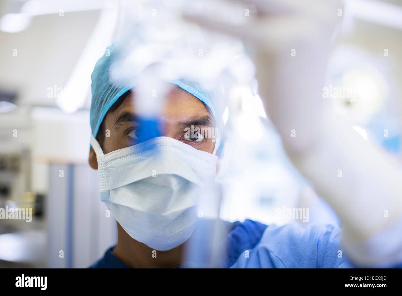 Chirurgo indossando mascherina chirurgica, cappuccio e guanti guardando flebo IV Foto Stock