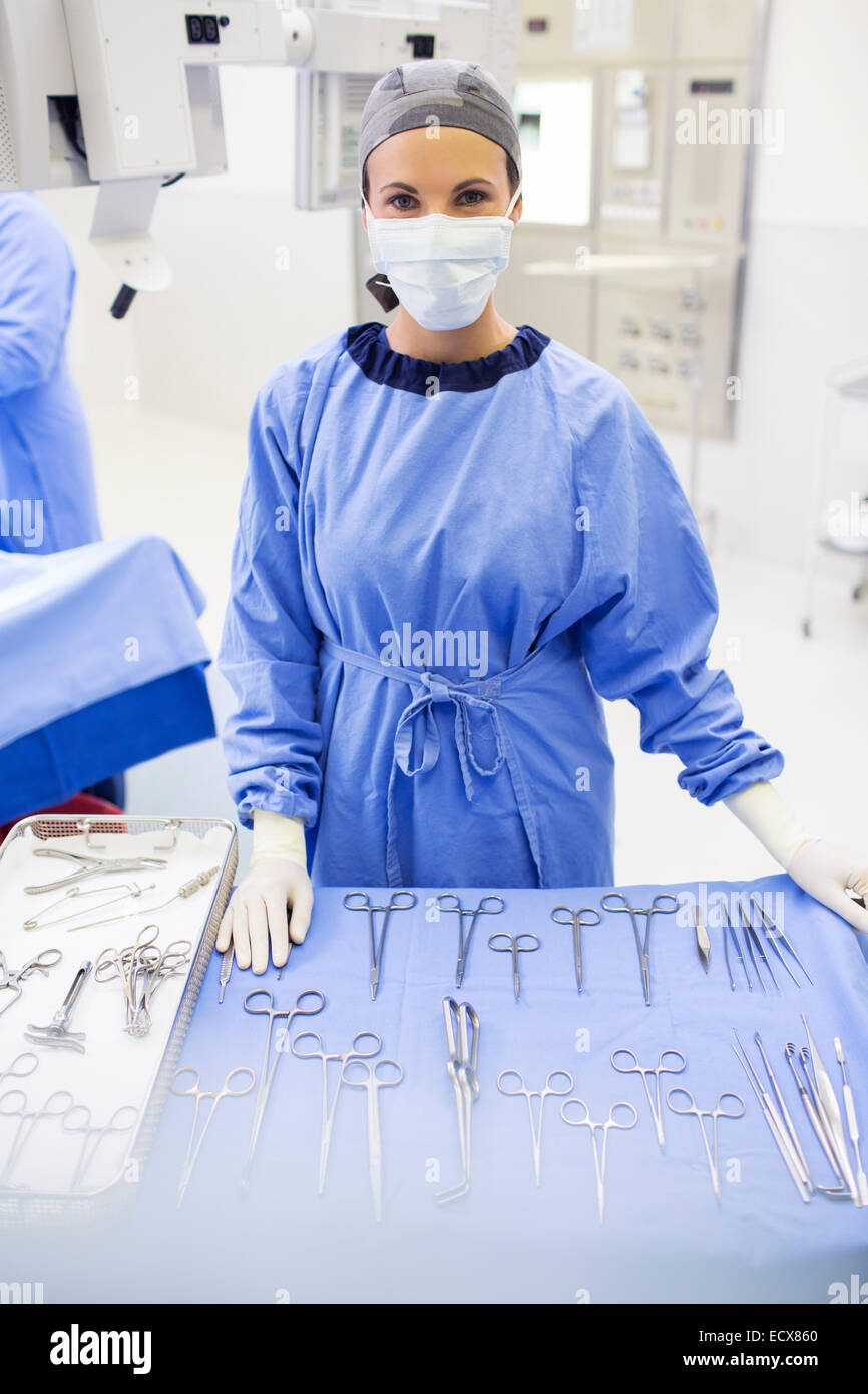 Ritratto di infermiere chirurgico in piedi dietro gli strumenti medici sul tavolo in sala operatoria Foto Stock