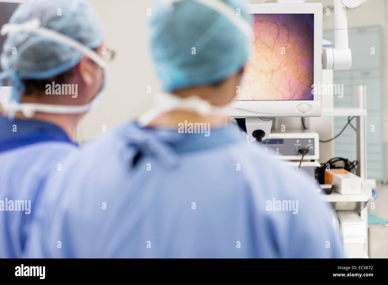 Vista posteriore di due chirurghi guardando il monitor durante un intervento chirurgico in sala operatoria Foto Stock