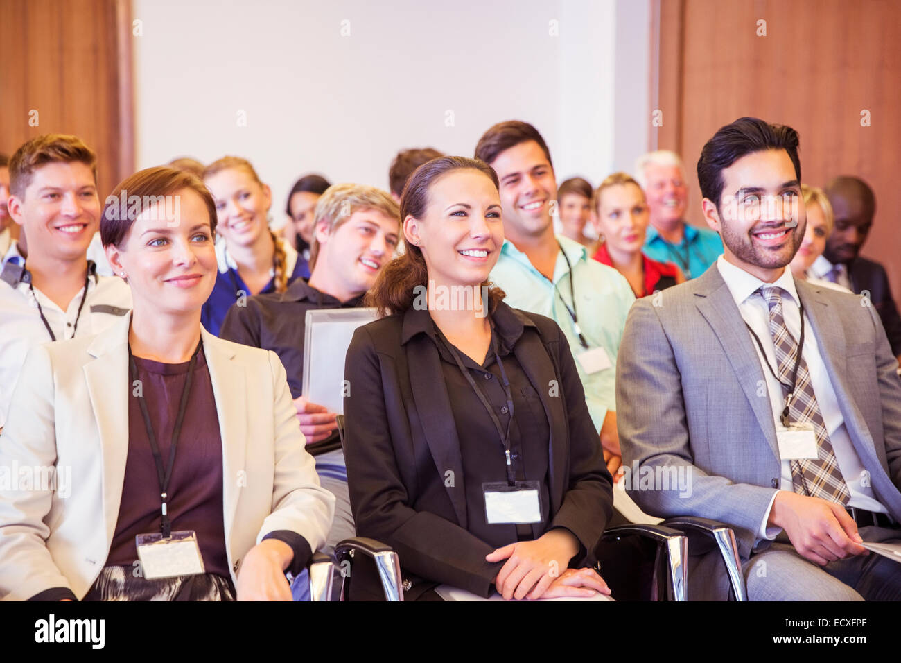 La gente di affari seduti nella sala conferenze, sorridente e guardando lontano Foto Stock