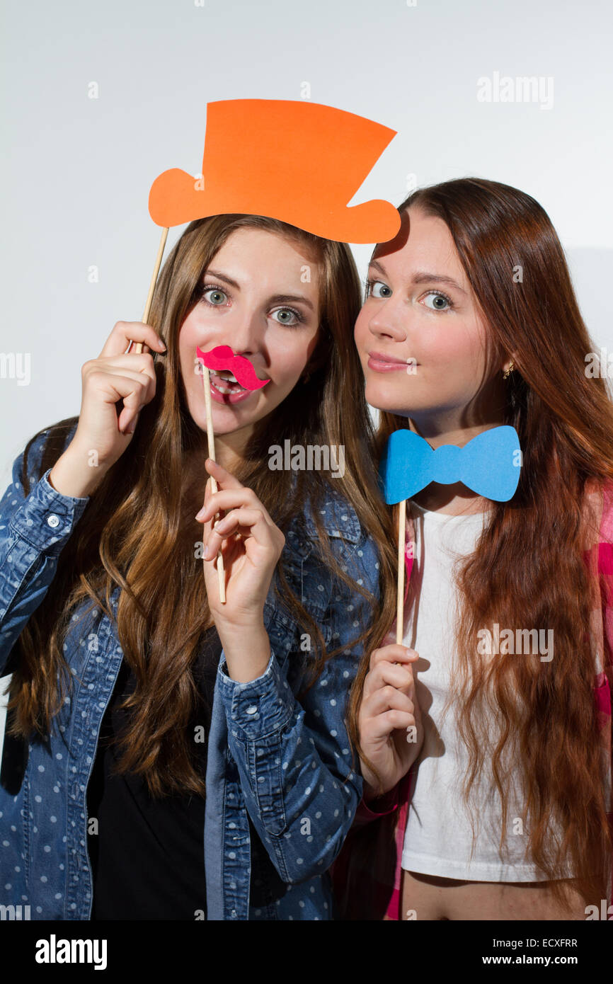 Due giovani donne godendo con sciocche puntelli che posano per una foto Photo Booth style Foto Stock
