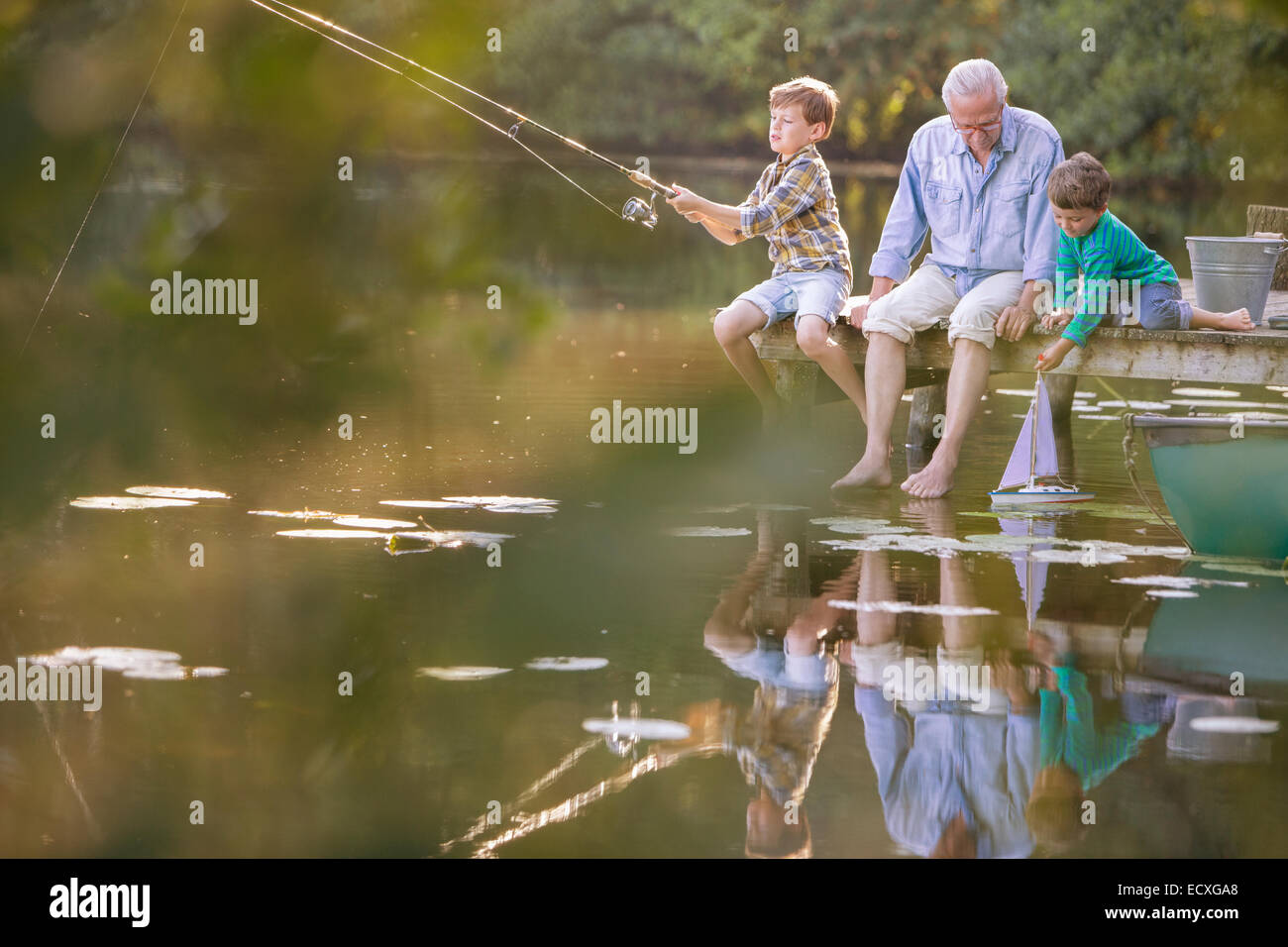 Nonno e nipoti la pesca e giocare con il giocattolo in barca a vela sul lago Foto Stock