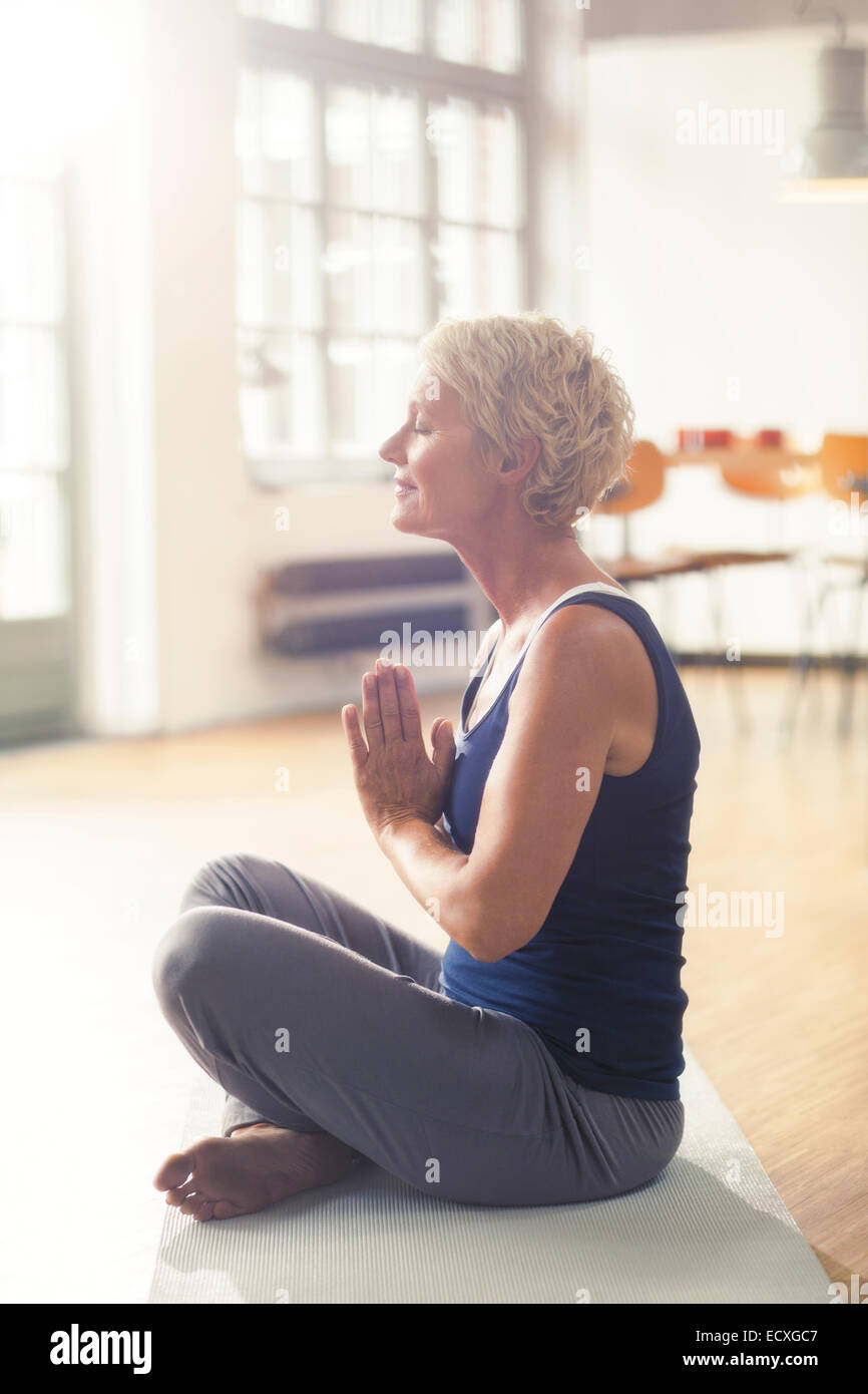 Donna anziana meditando sul tappeto di esercizio Foto Stock