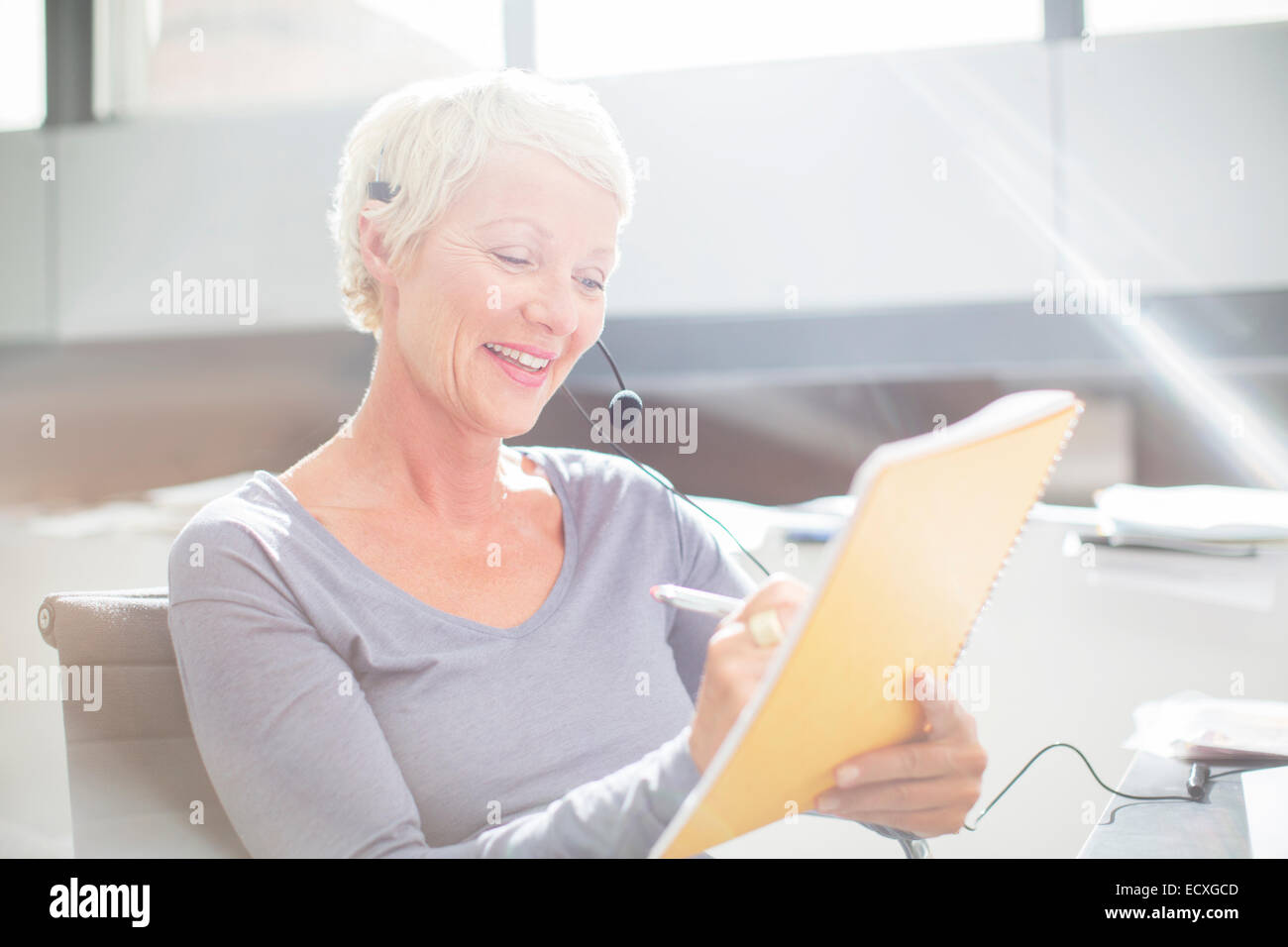 Imprenditrice in cuffia la scrittura sul blocco note in Office Foto Stock