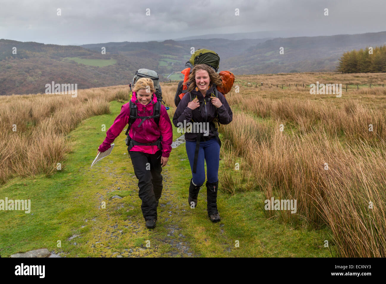 Due sorridente camminatori femmina su una pista sulle pendici del Moel Siabod in condizioni di tempo piovoso, Capel Curig, Gwynedd, Galles del Nord, Regno Unito Foto Stock