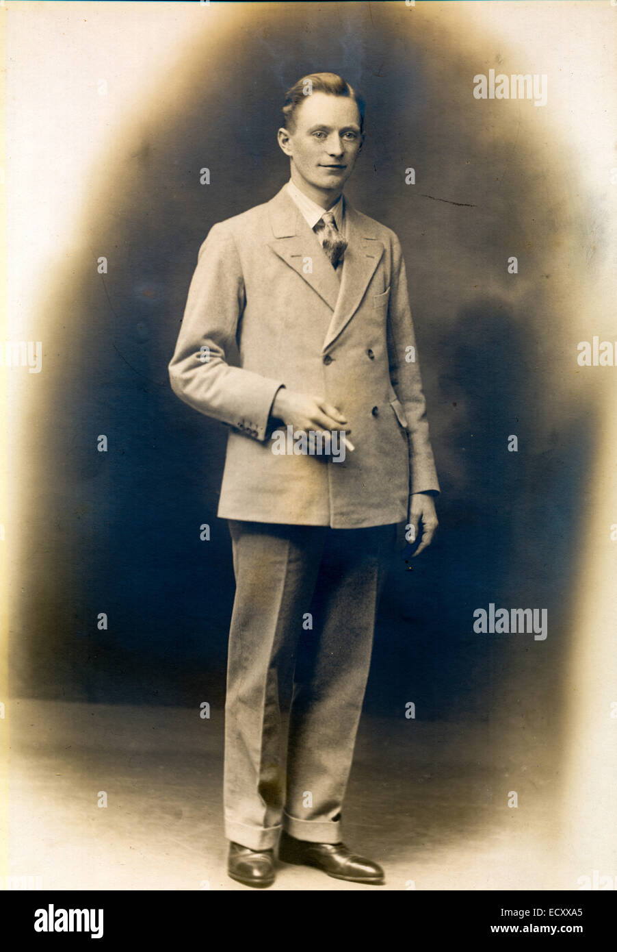 Circa 1920 seppia colorato studio ritratto di Ciril Fairman, leader della band. Giovane uomo in tuta, in piedi, tenendo la sigaretta, guardando lo spettatore. Foto Stock