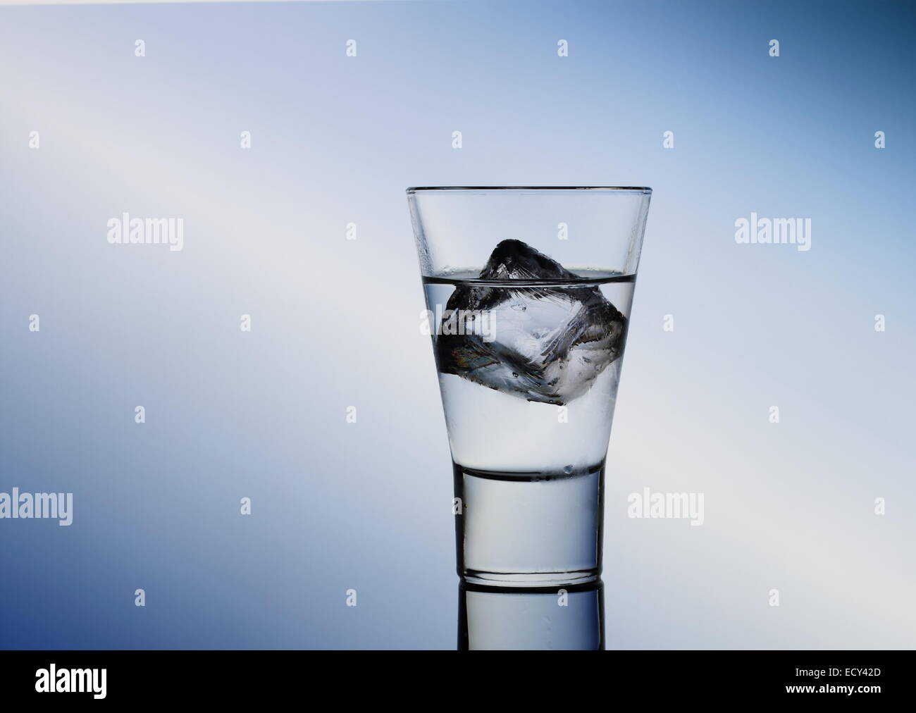 Short drink di vetro con liquido chiaro e cubetti di ghiaccio, sfondo blu Foto Stock