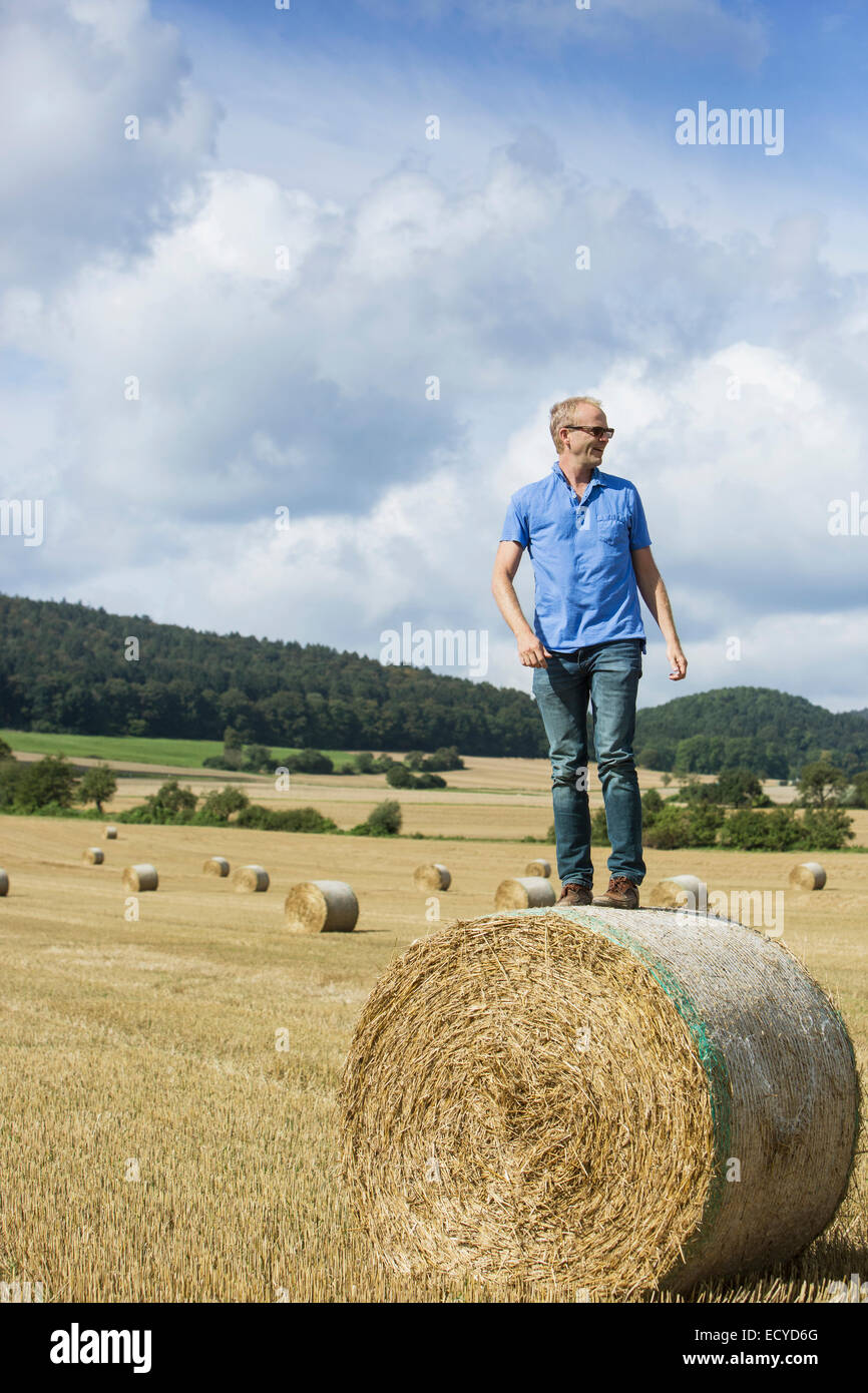 Agricoltore permanente sulla balla di fieno nel campo Foto Stock