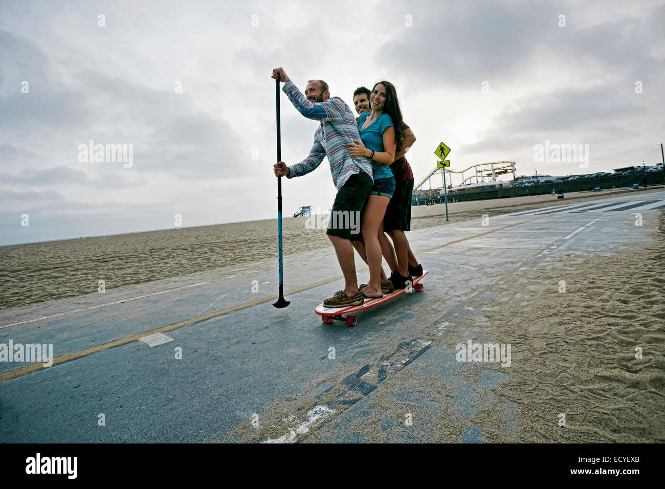 Gli amici lo skateboard con paddle polo alla spiaggia Foto Stock