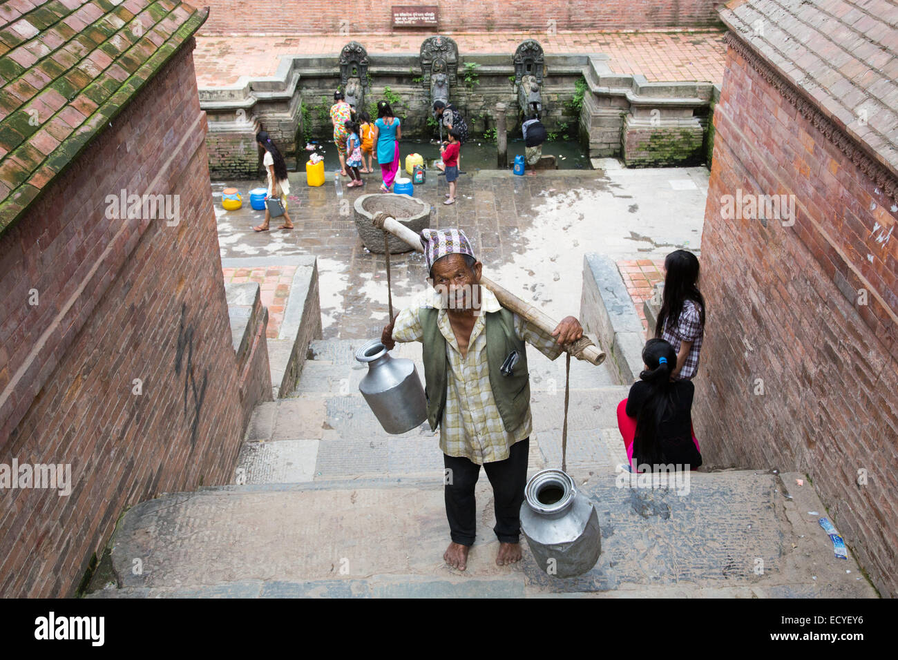 Uomo nepalese che trasportano l'acqua da un pozzo in Patan Durbar Square, Kathmandu, Nepal Foto Stock