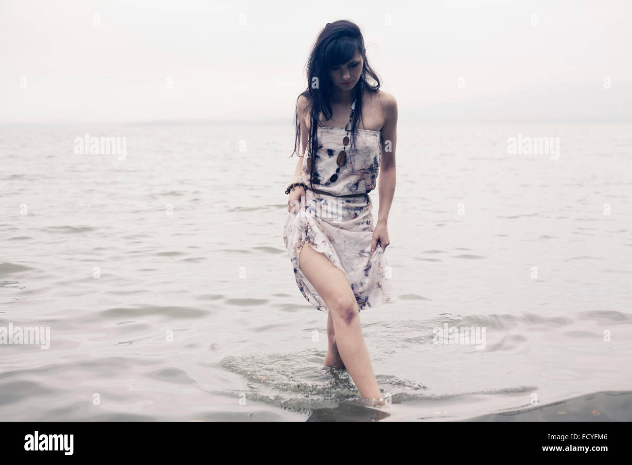 La donna caucasica guadare in acqua sulla spiaggia Foto Stock