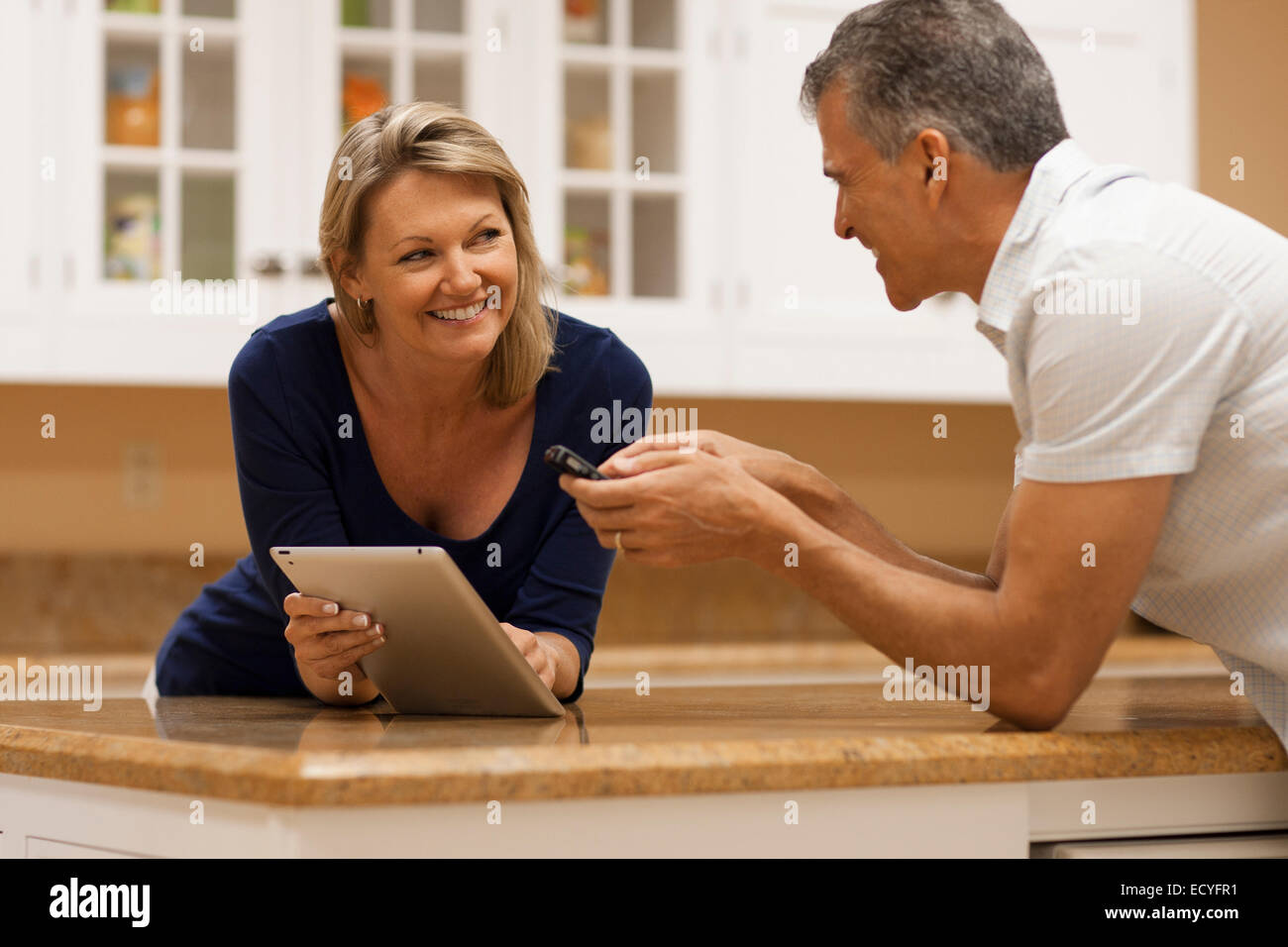 Coppia caucasica utilizzando tavoletta digitale e telefono cellulare a banco di cucina Foto Stock