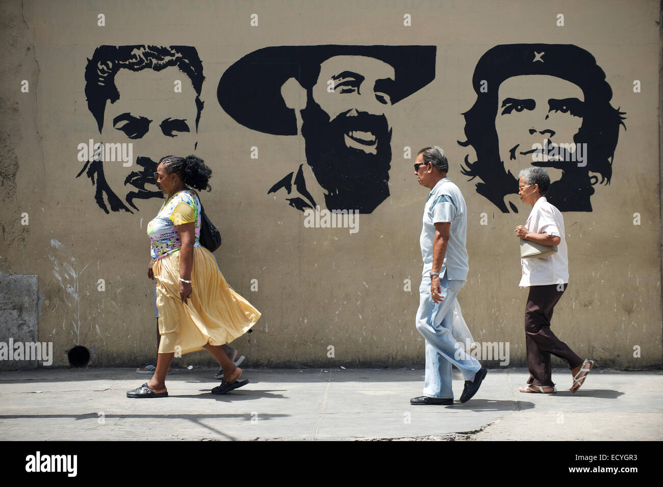 L'Avana, Cuba - 16 Maggio 2011: il popolo cubano a piedi nella parte anteriore del cartellone con i rivoluzionari Mella, Cienfuegos e Guevara. Foto Stock