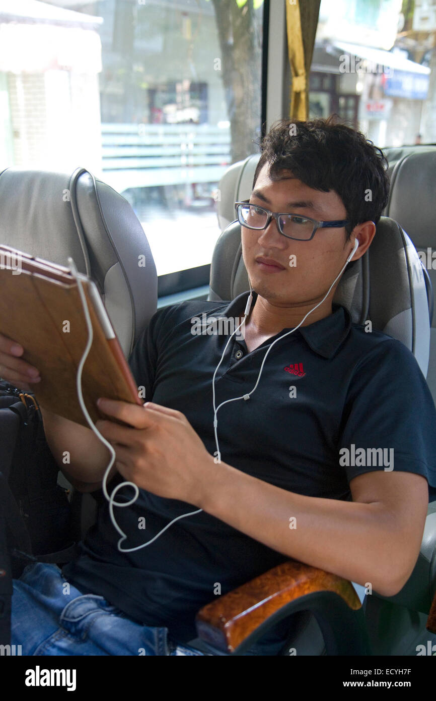 Giovane vietnamita uomo che utilizza un computer tablet su un bus ad Hanoi, Vietnam. Foto Stock
