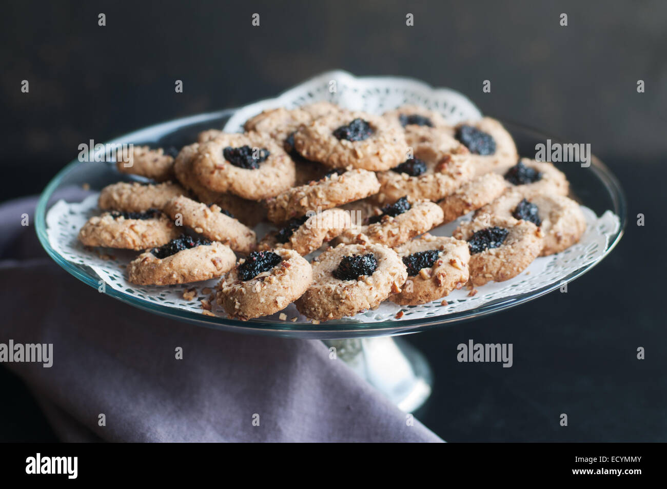 Pollice inceppamento stampa cookie visualizzati sul vetro piatto torta con il bianco centrini e asciugamano viola Foto Stock