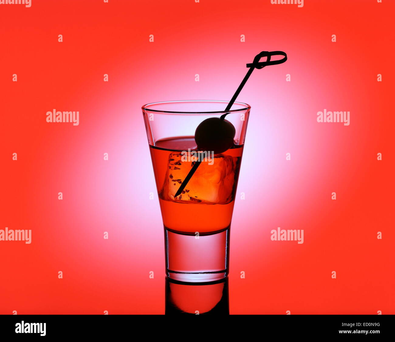 Short drink di vetro con liquido rosso e verde oliva, sfondo rosso Foto Stock