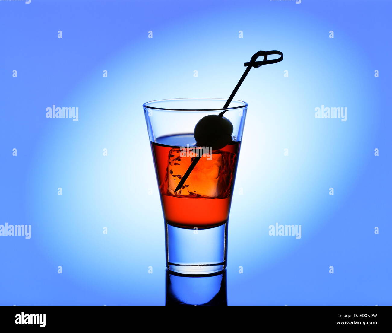 Short drink di vetro con liquido rosso e verde oliva, sfondo blu Foto Stock