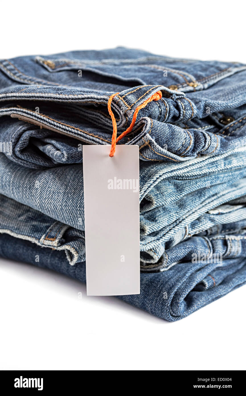 Pila di jeans blu con etichetta isolati su sfondo bianco. Messa a fuoco selettiva su etichetta della tag. Foto Stock