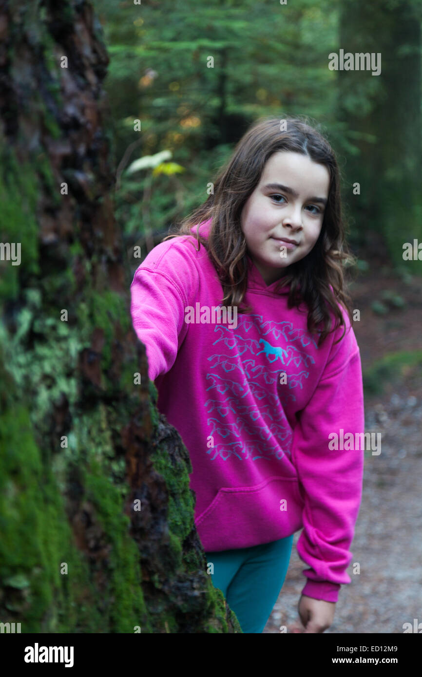 Ragazza giovane guardando da dietro un grande albero in una foresta pluviale temperata Foto Stock