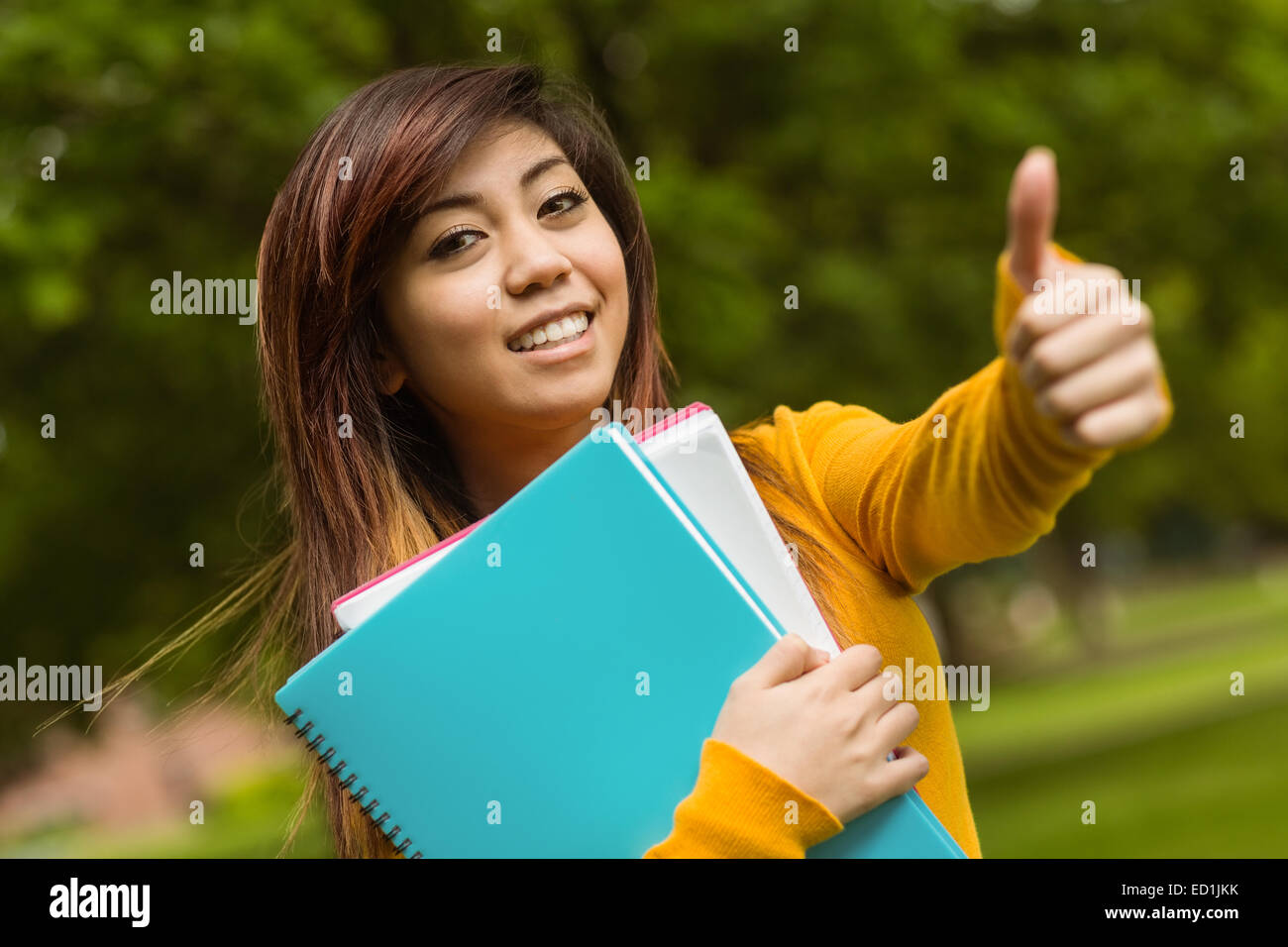 Studente di college con libri gesticolando pollice in alto in posizione di parcheggio Foto Stock