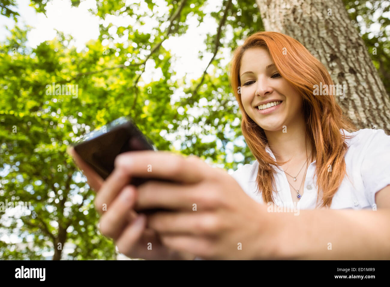 Pretty redhead la messaggistica di testo sul suo telefono Foto Stock