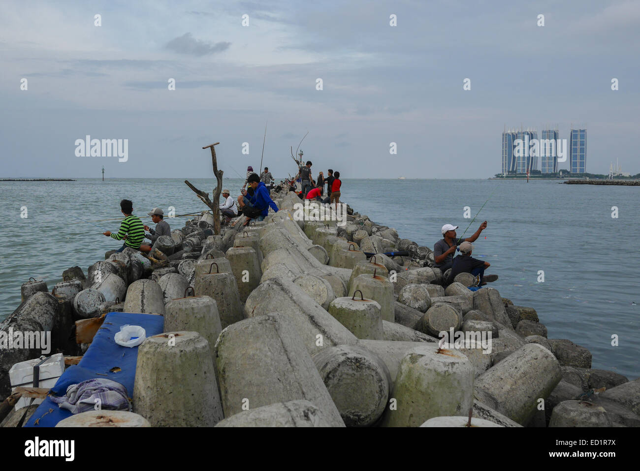 Persone che pescano da strutture di tetrapod, che stanno proteggendo il porto di pesca di Muara Angke come rompigonda a Penjaringan, Jakarta, Indonesia. Foto Stock