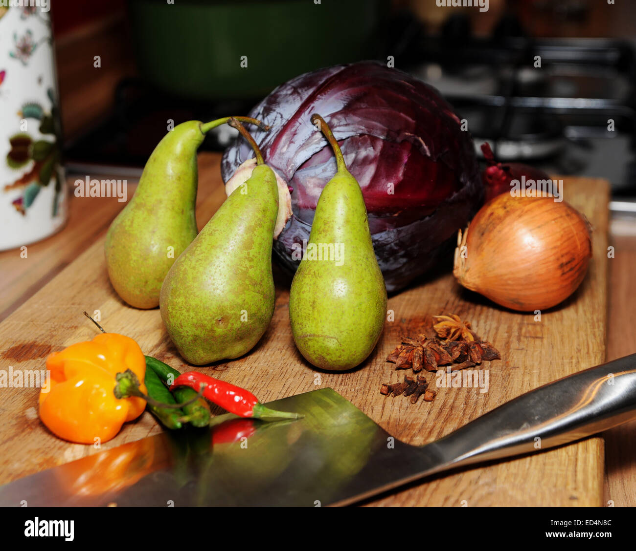 Ingredienti per spiced cavolo rosso con pere anice stellato e i chiodi di garofano e una cipolla bianca sul tagliere con vari peperoncini rossi Foto Stock