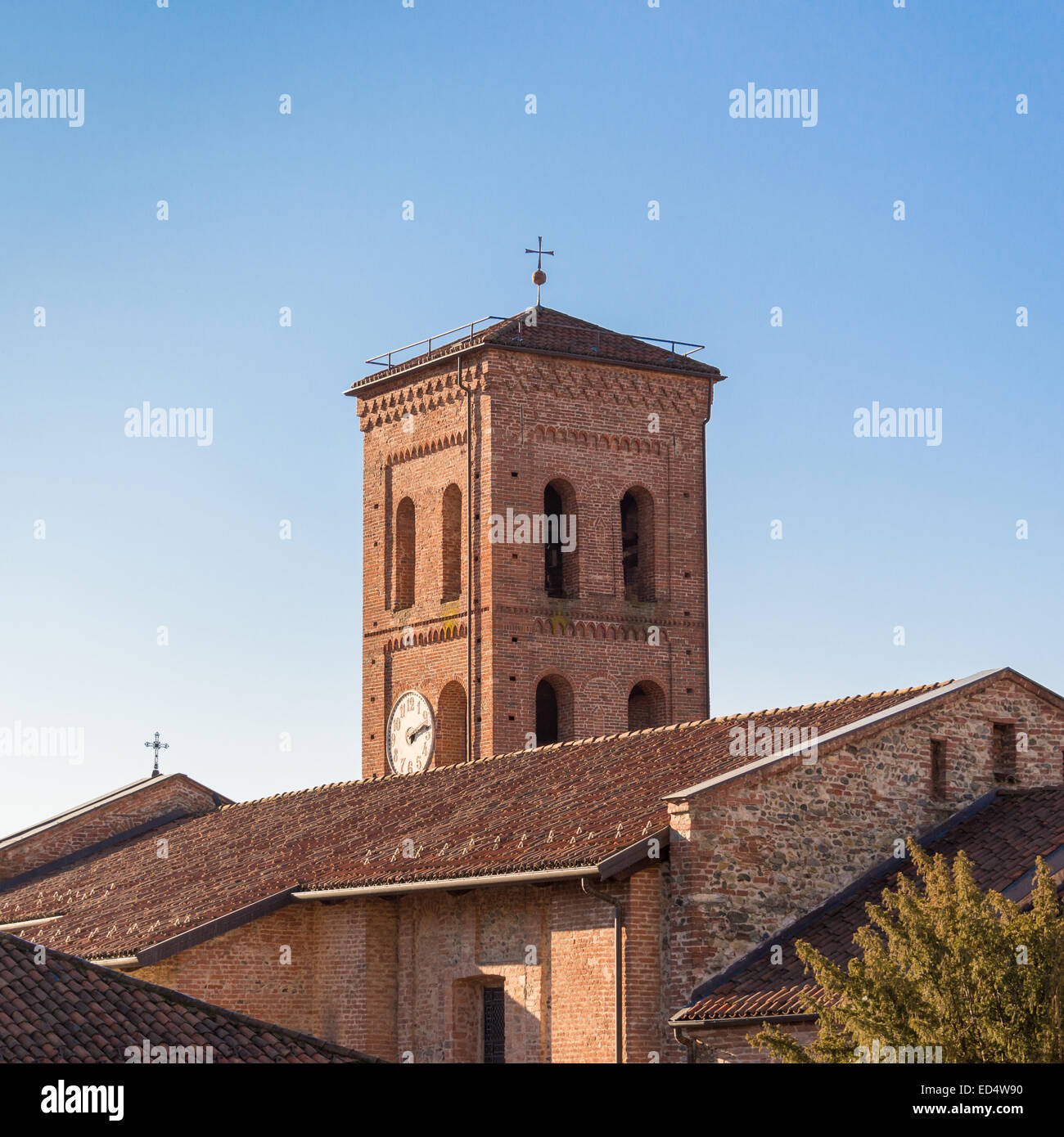 Piacevole vista del campanile di una romanica chiesa cattolica in Italia, con il tetto della chiesa e il bellissimo cielo blu chiaro Foto Stock