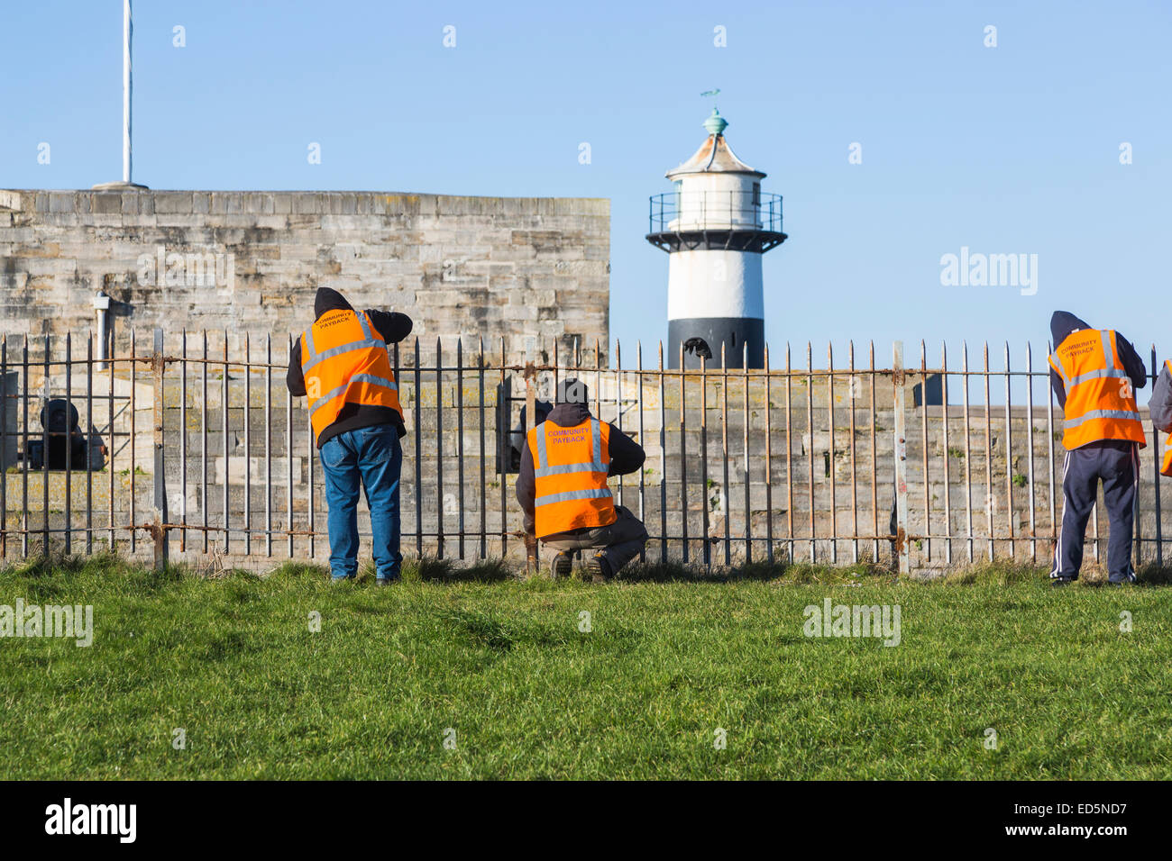 I trasgressori funzionante a Southsea Castle, Portsmouth, effettuare il servizio comunitario; arancione giacche inscritto " Comunità " di reintegrazione del capitale investito Foto Stock