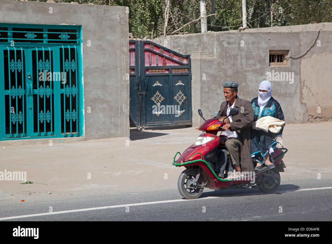 Uyghur uomo nel tradizionale abito musulmana, il bambino e la moglie indossa velo islamico a cavallo su uno scooter, provincia dello Xinjiang, Cina Foto Stock