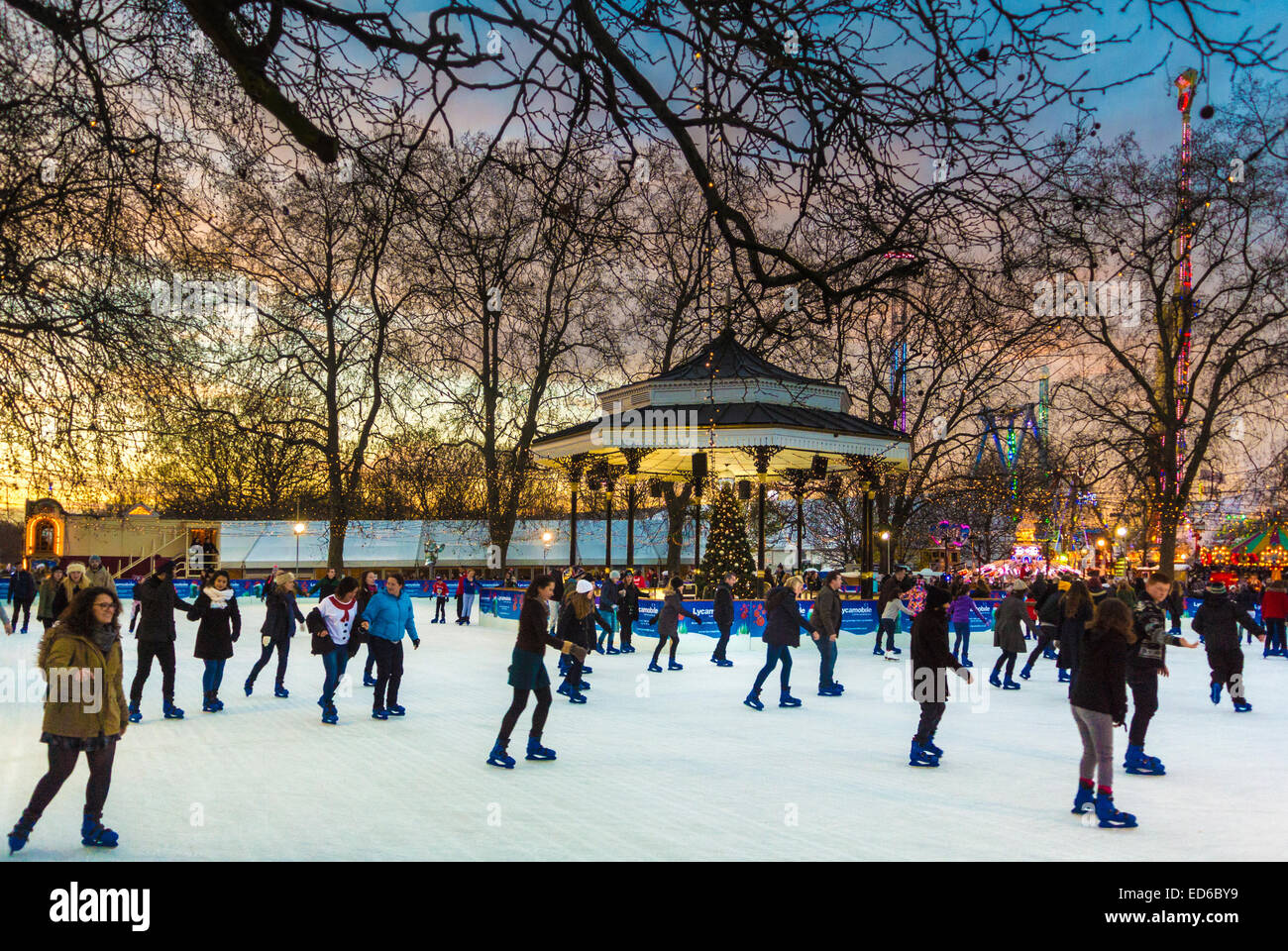 Pattinatori sulla pista di pattinaggio intorno al banco del palco di Hyde Park Winter Wonderland, al tramonto. Londra Foto Stock