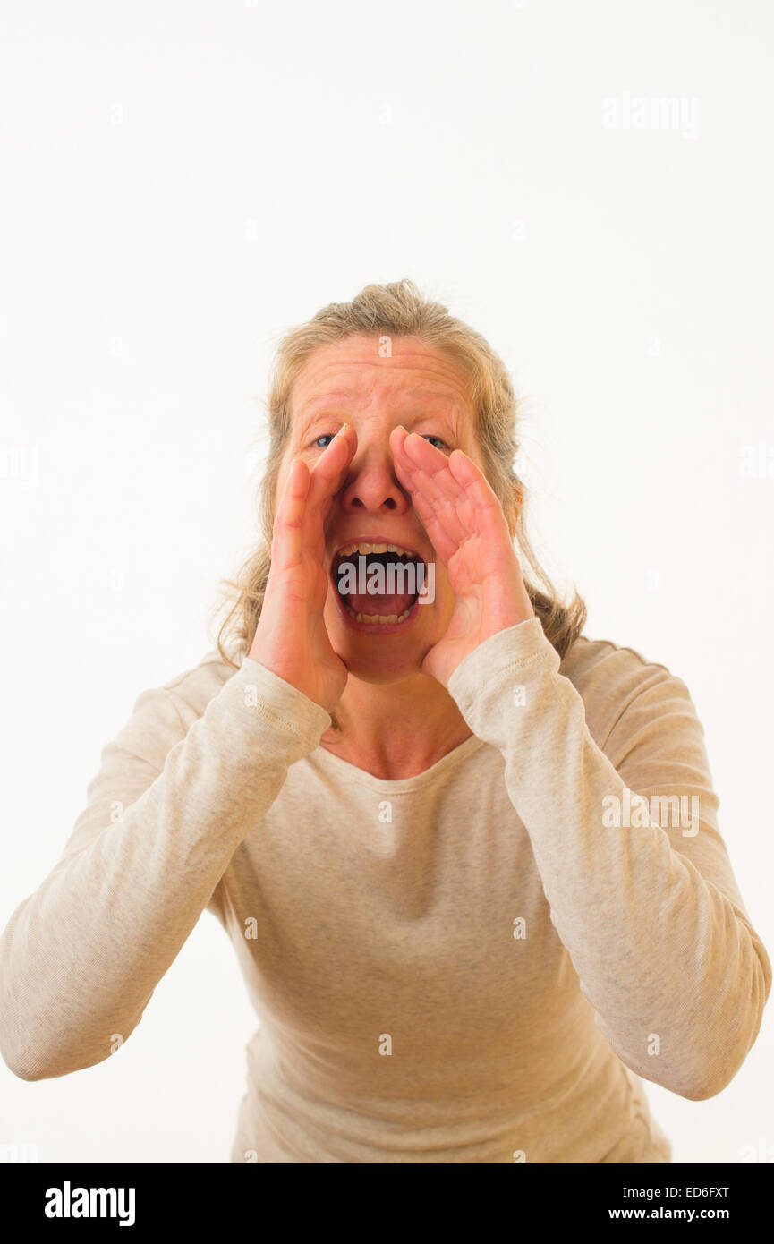 Un quarantenne donna caucasica grida urla attraverso le sue mani a tazza contro uno sfondo bianco. Regno Unito Foto Stock