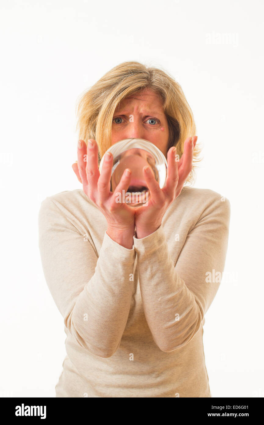 Guardando al futuro: un quarantenne adulto donna caucasica guardando inorridito preoccupato spaventata al suo futuro in guardando nella sfera di cristallo tenuto nelle sue mani contro uno sfondo bianco. Regno Unito Foto Stock