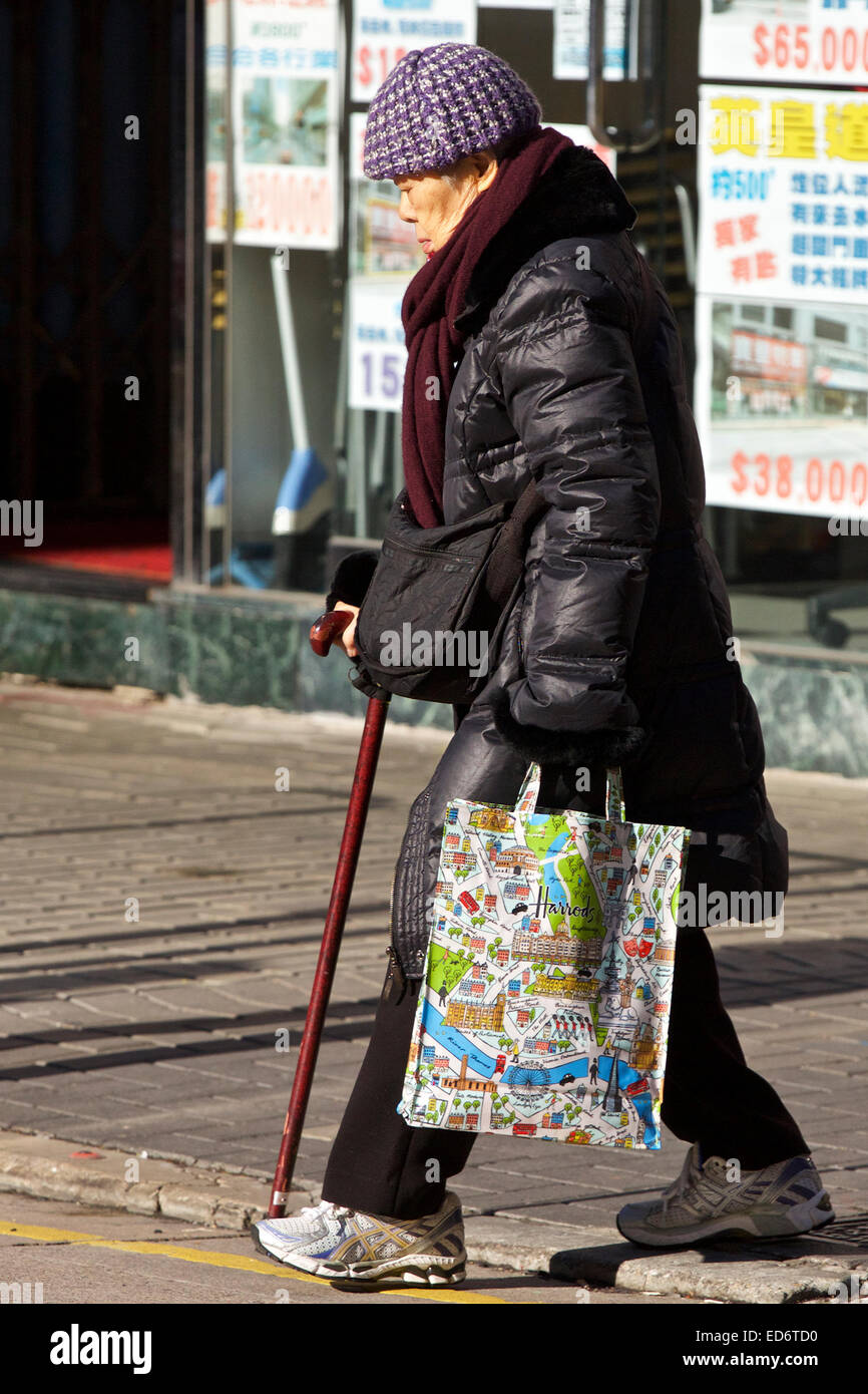 Anziani donna cinese attraversando la strada a Hong Kong durante l'inverno. Foto Stock