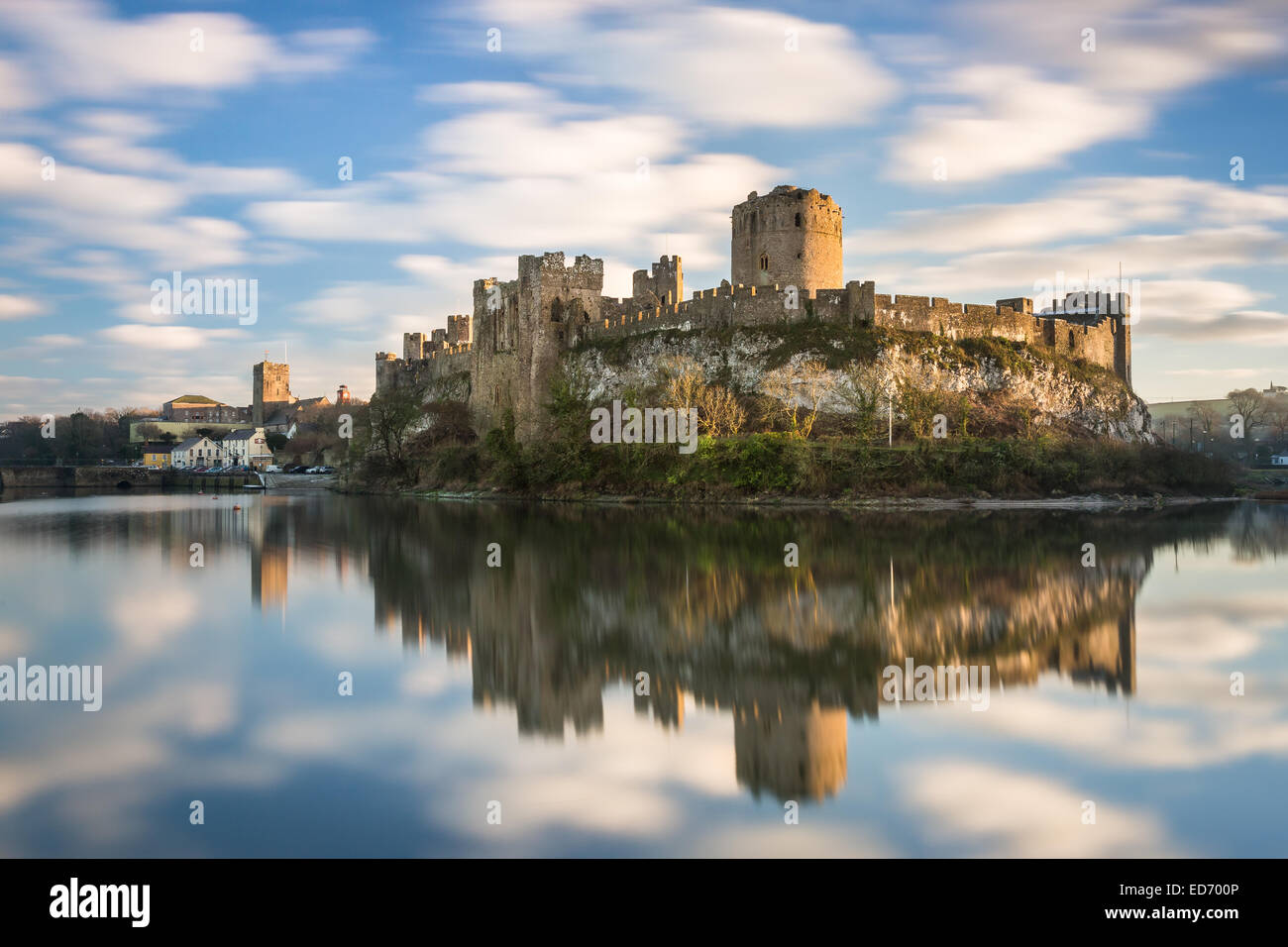 Pembroke Castle al tramonto con riflessi nel fossato mill pond. Una lunga esposizione a sfocatura movimento delle nuvole e castello fanno risaltare Foto Stock