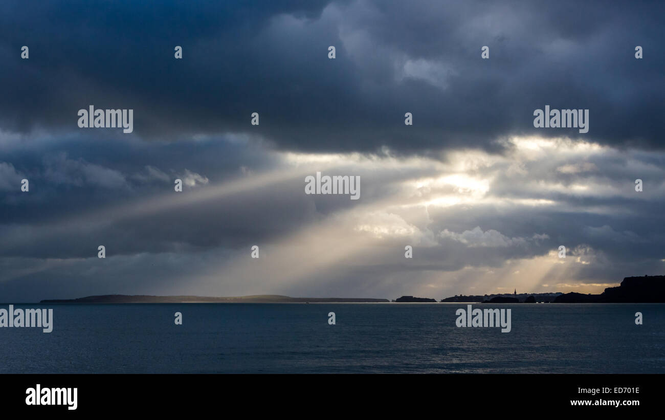 Crepuscolare raggi di sole risplendere in giù su Tenby, Tenby Harbour e isola di Caldey su Il Pembrokeshire Coast. Fotografato da Amroth Foto Stock