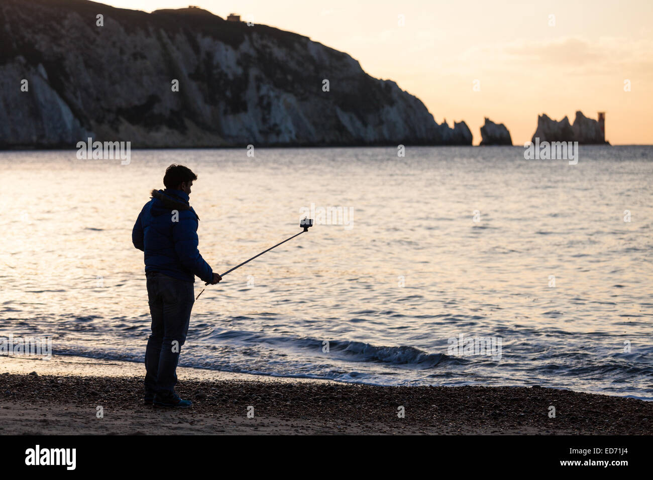 Un uomo con un 'selfie stick' ad Alum Bay sull'Isola di Wight con gli aghi nella distanza Foto Stock
