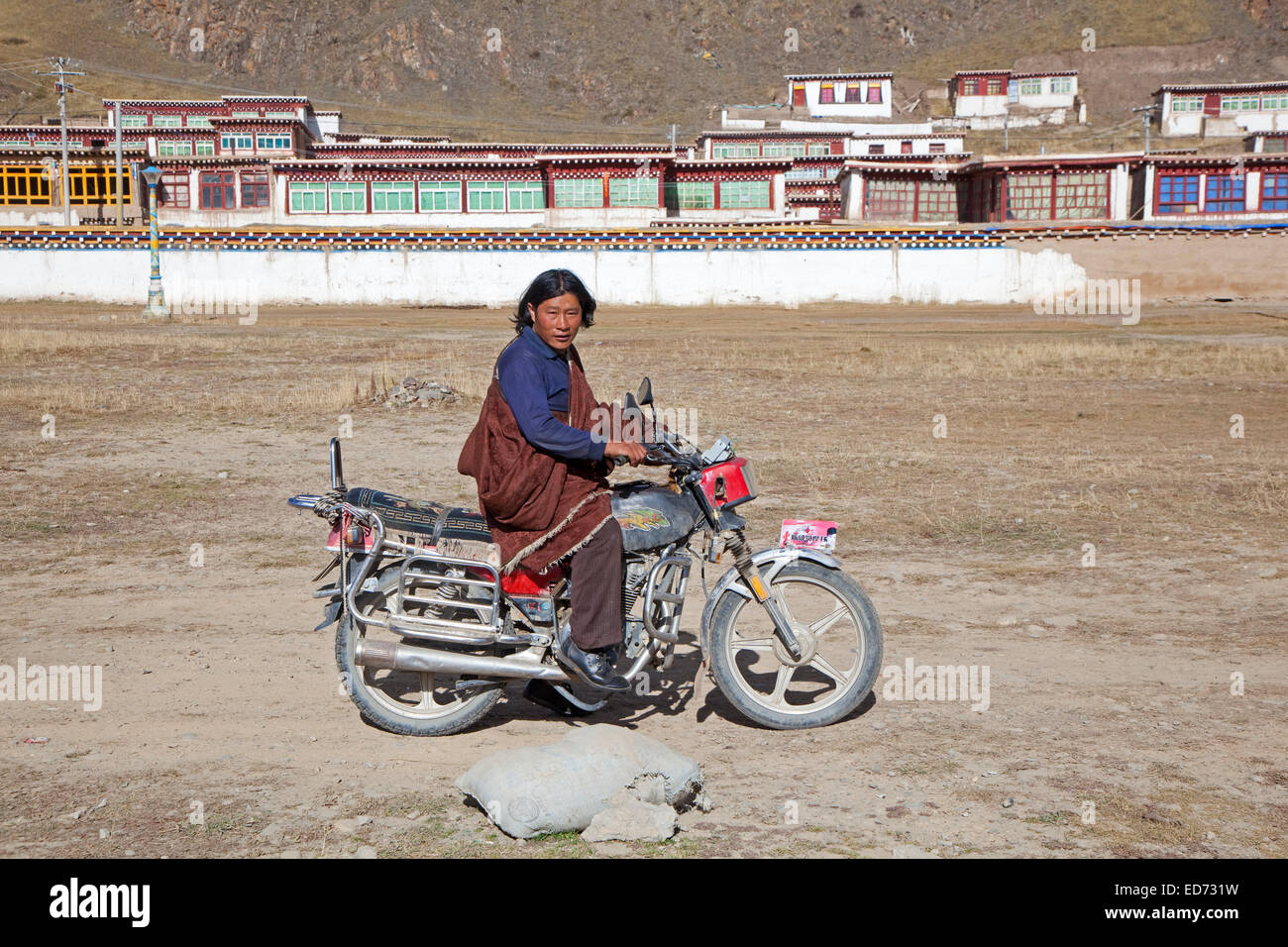 Uomo tibetano in sella moto nella parte anteriore del monastero tra Sershu Dzong e Sershu / Serxu, nella provincia di Sichuan, in Cina Foto Stock