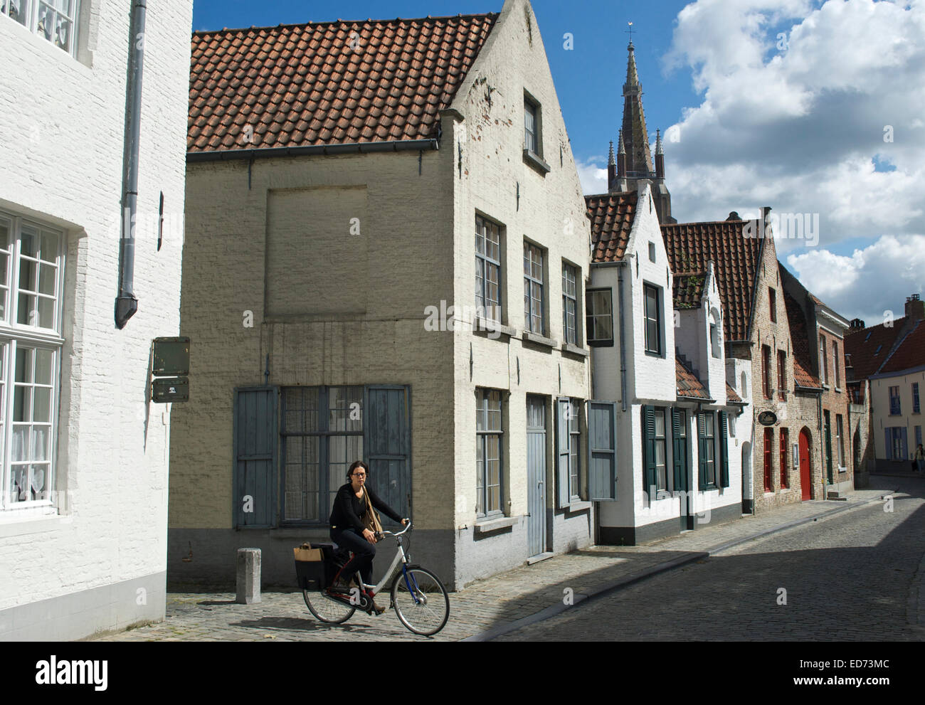 Una donna in bicicletta nella parte anteriore del medioevo una fila di case su una strada di Bruges, Belgio, Europa Foto Stock