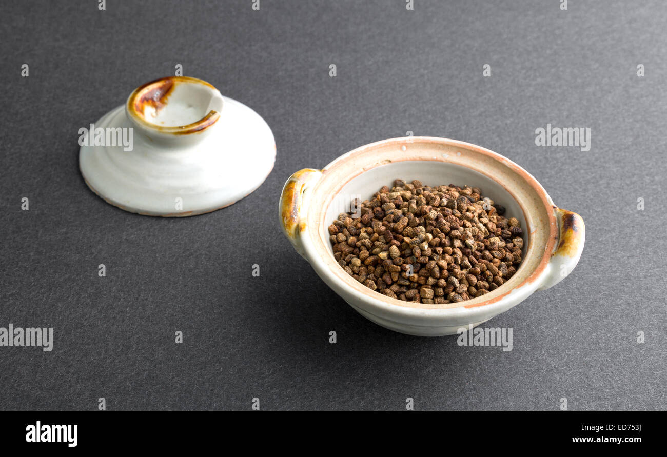 Una porzione di semi di cardamomo in una piccola ciotola con il coperchio in background. Foto Stock