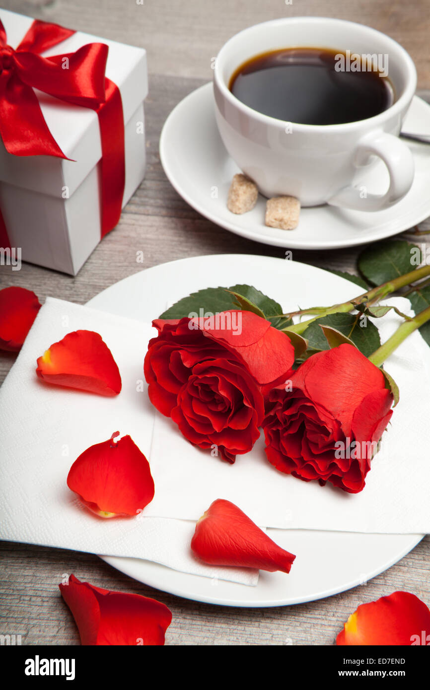 Rose rosse, una tazza di caffè e presente su un tavolo Foto Stock